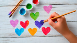Child&rsquo;s hand painting colorful hearts with brush and watercolors
